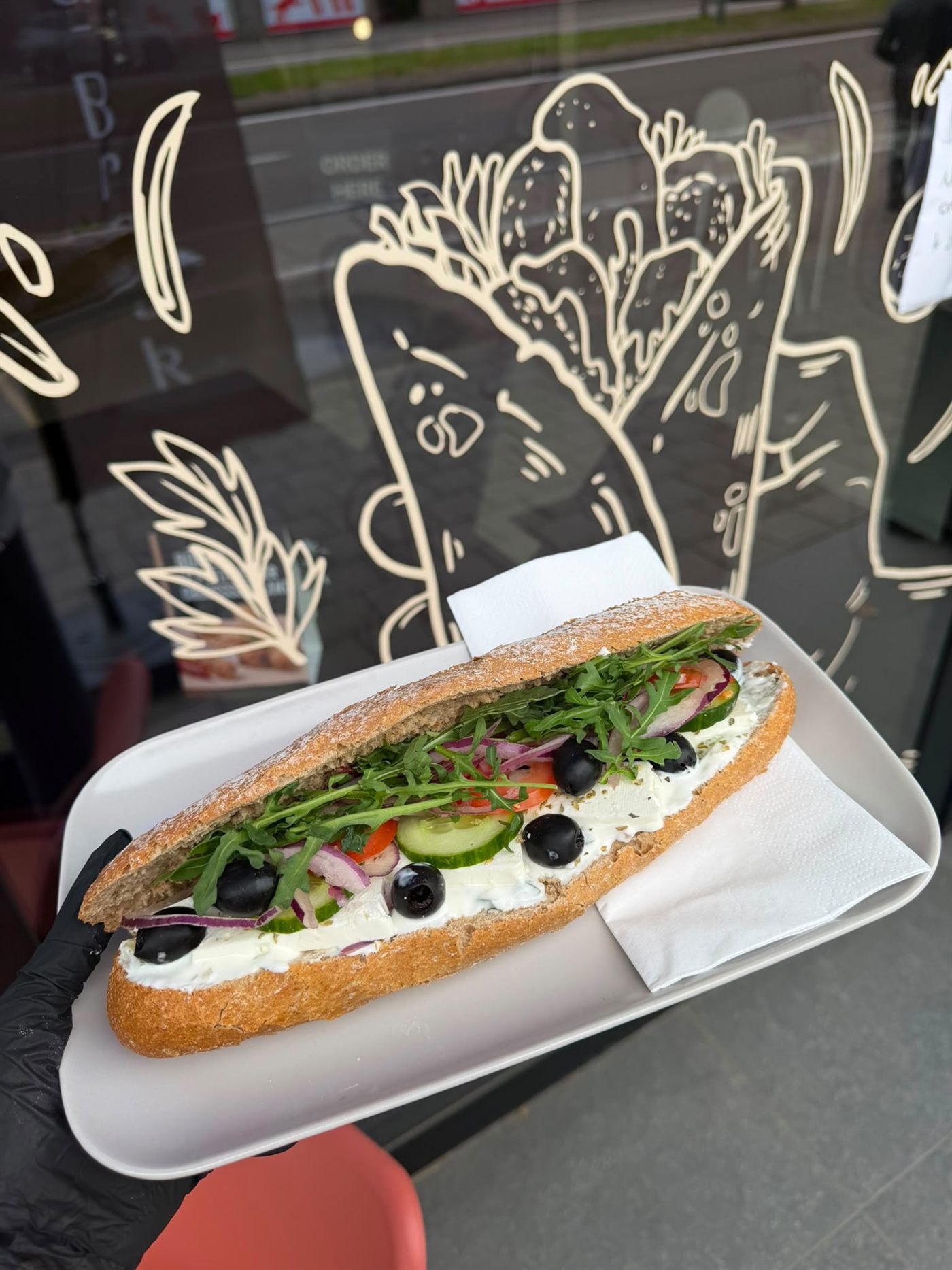 Bruin broodje met roomkaas, olijven en rucola voor het raam